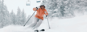 Een skiër in een oranje jas staat op de piste.
