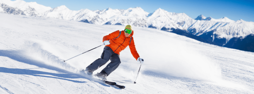 Een man op ski's op wintersport in een oranje jacket. Deze foto staat bij de blog van VHD over de voorjaarsvakantie.